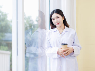 Portrait confident asian professional female doctor wearing white coat stand with coffee relax leaning against window looking at view clinic office hospital healthcare medical services consultation.