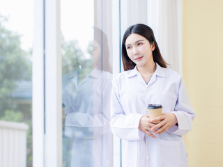 Portrait confident asian professional female doctor wearing white coat stand with coffee relax leaning against window looking at view clinic office hospital healthcare medical services consultation.
