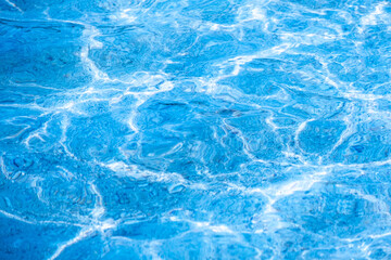 Close-up of bright blue swimming pool water surface with sunlight reflections and ripples, refreshing summer vacation and tropical luxury background.concept relex