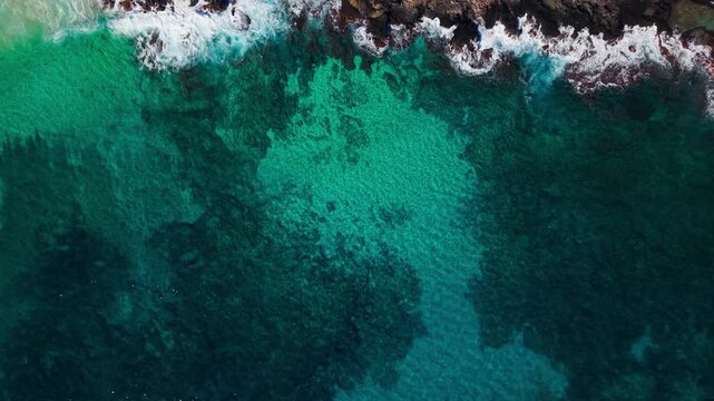 Top-down aerial drone video of turquoise ocean water over coral reef with waves breaking along the shoreline, abstract tropical seascape with natural patterns and vibrant coastal colors