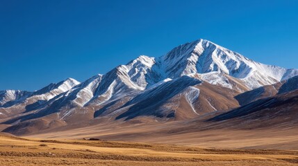 Arid mountain valley under a blue sky; snow-capped peaks rise above ochre dunes and distant plains. At horizon