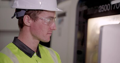Young caucasian male technician wearing safety gear focusing on control panel during machine operation in smart factory environment under automation training program