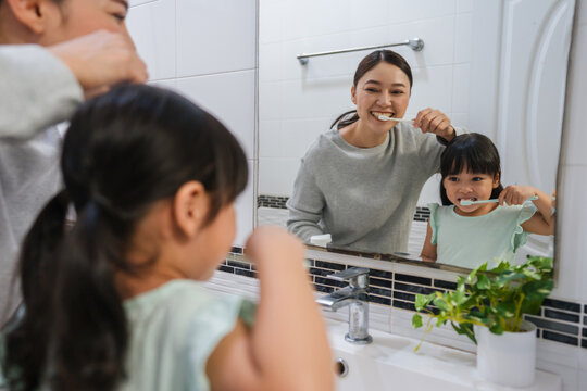 mother teaching girl child to brushing teeth at reflection in mirror in bathroom