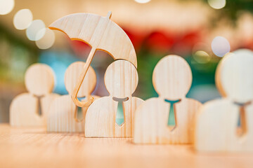 Wooden human figure holding umbrella to protect others, representing insurance, protection, care,...