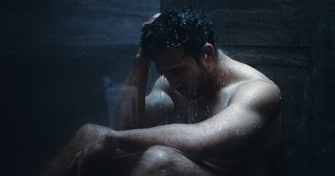 Man, shower and frustrated in bathroom for grief, mental health and reflection in home. Person with depression, house and running water with emotions, fear and disappointed with anxiety or stress