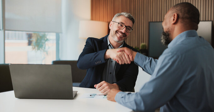 Shaking hands, agreement and business men in office for finance partnership, deal or collaboration. Happy, laptop and male financial advisor with client for investment contract with handshake.