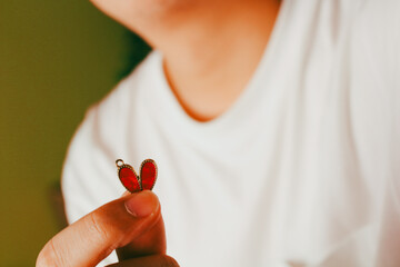 Close up of man hand holding a small red heart pendant over white shirt background, concept of love, relationship, valentine's day and broken heart.