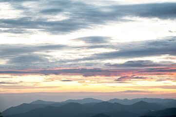 Obraz premium Landscape sunrise near Ooty, Nilgiris showing layered mountain silhouettes emerging through mist on a monsoon morning, with a cloudy sky glowing in soft yellow, orange, black and pink gradients.