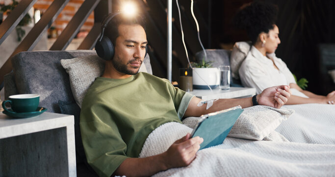 Headphones, man and tablet with drip therapy in lounge for nutrients, recovery or streaming app. Flare, patient and tech with IV vitamin c for health benefits, mineral infusion or immune system boost