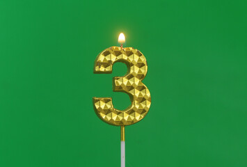 Burning gold birthday candle on green background, number 3