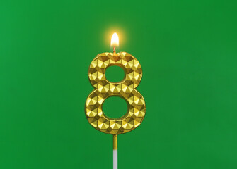 Burning gold birthday candle on green background, number 8