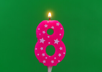 Burning pink with white stars birthday cake candle on green background. Number 8.