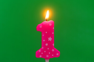Burning pink with white stars birthday cake candle on green background. Number 1.