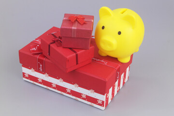 Yellow piggy bank with two gift boxes on grey. Saving money for gifts concept.	