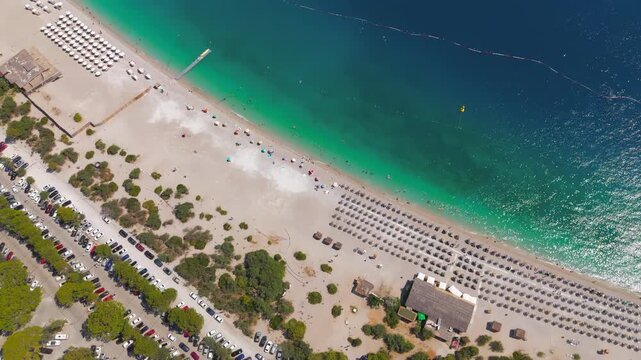 Oludeniz, Turkey. Aerial drone view of vibrant Oludeniz Beach with rows of colorful umbrellas, people on sunbeds, waves crashing on pebble shore, summer day.. Aerial View