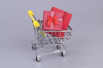Gift boxes in shopping cart on grey background. 