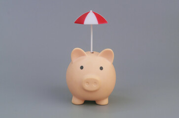 Piggy bank under umbrella on grey background. Money safety concept.