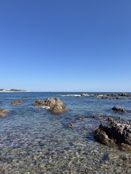 Crystal Clear Ocean Water with Coastal Rocks and Blue Sky, Serene Summer Beach Landscape