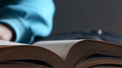 Close-up of male hands turning book page, nestled atop stacked volumes in soft, muted library setting, creating intimate reading environment, selective focus.