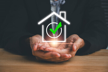 Businessman holding a digital house icon with a checkmark, symbolizing real estate approval, security, and investment.
