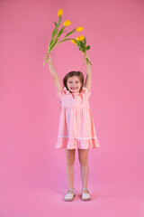 funny girl in pink dress with yellow tulips flower on pink background.