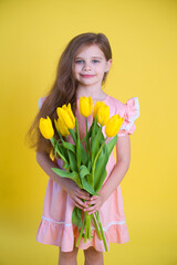 Cheerful happy girl with tulips flower bouquet in pink dress on yellow background