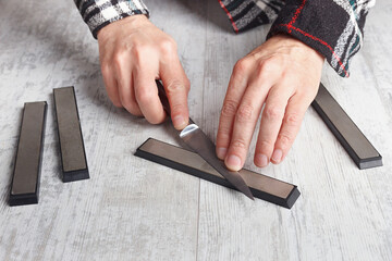Sharpening small kitchen knife on white table.