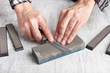 Sharpening small hunting on whetstone knife on white table.