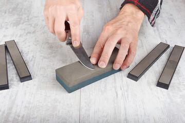 Manual sharpening hunting knife on whetstone on white table.