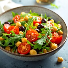 A bowl of salad with tomatoes, chickpeas, and greens on a table