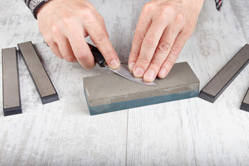 Manual sharpening fishing knife on whetstone on white table.