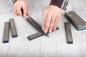 Sharpening big kitchen knife on white table.