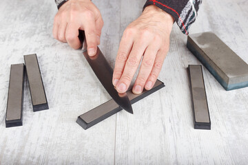 Sharpening big carving kitchen knife on whetstone on white table.
