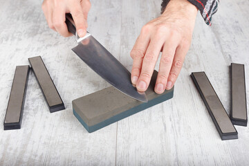 Professional sharpening chef's knife on whetstone on white table.