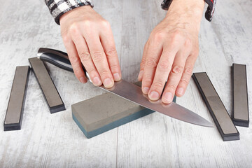 Manual sharpening big kitchen knife on whetstone on white table.