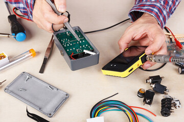 Serviceman checks board of electrical device with compact oscilloscope at service workplace.