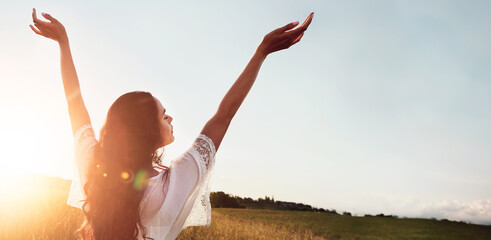 Fototapeta premium Holiday, back and woman at field for freedom on adventure, calm and breathing in countryside. Arms up, meadow and person in nature on getaway trip at sunset with flare, mockup space and peace outdoor