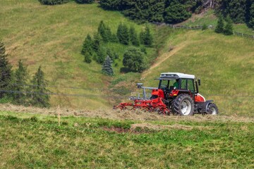 Fototapeta premium Tractor with attached tedder working hay on alpine slope