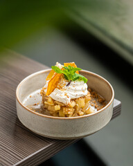 A sophisticated dessert featuring a base of diced caramelized apples, topped with a swirl of fresh whipped cream, citrus zest, and mint leaf, served in a modern ceramic bowl at a fine dining restauran © Simone Oppes