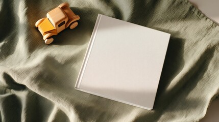 Minimalist children's book mockup with wooden toy on fabric background