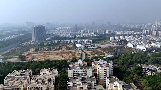 Aerial view of Greater Noida under light haze, showing expanding residential sectors, open development land, and emerging high-rises amid NCR&rsquo;s rapid urban growth.