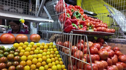 Zoom-out shot of fresh vegetables at a produce market, colorful bell peppers, hot chilli peppers (ajies), and tomatoes displayed together, vibrant healthy food and local market scene.