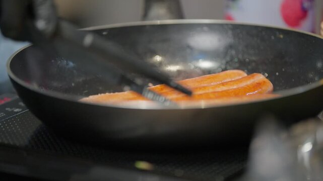 Row of juicy sausages being pan-fried in a professional kitchen setting