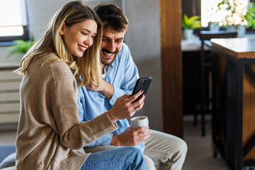 Happy couple relaxing at home with coffee, enjoying online shopping and shared digital experiences