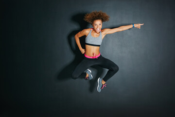 Dance, jump and portrait of woman in dark studio for choreography, energy or fitness routine. Exercise, pointing and space with hip hop dancer on black background for hobby, practice or rehearsal