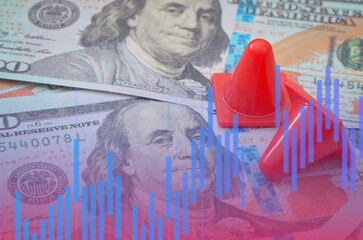 Financial warning concept with red traffic cones on hundred-dollar bills and blue stock market chart overlay.