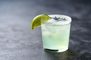 Margarita cocktail with ice cubes in glass and lime on a black table with copy space for text.