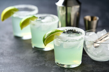 Many glasses of Margarita cocktail in a line , selective focus. Three glasses in row with cocktail Margarita and fresh lime on a black table.