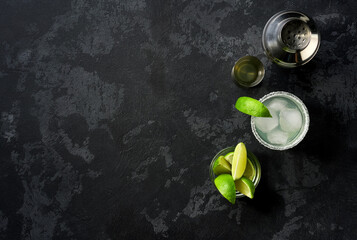 Margarita cocktail with ice cubes in glass and lime on a black table , top view.