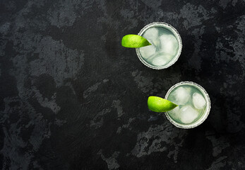 Two glasses of tasty Margarita cocktail on a black table, top view.